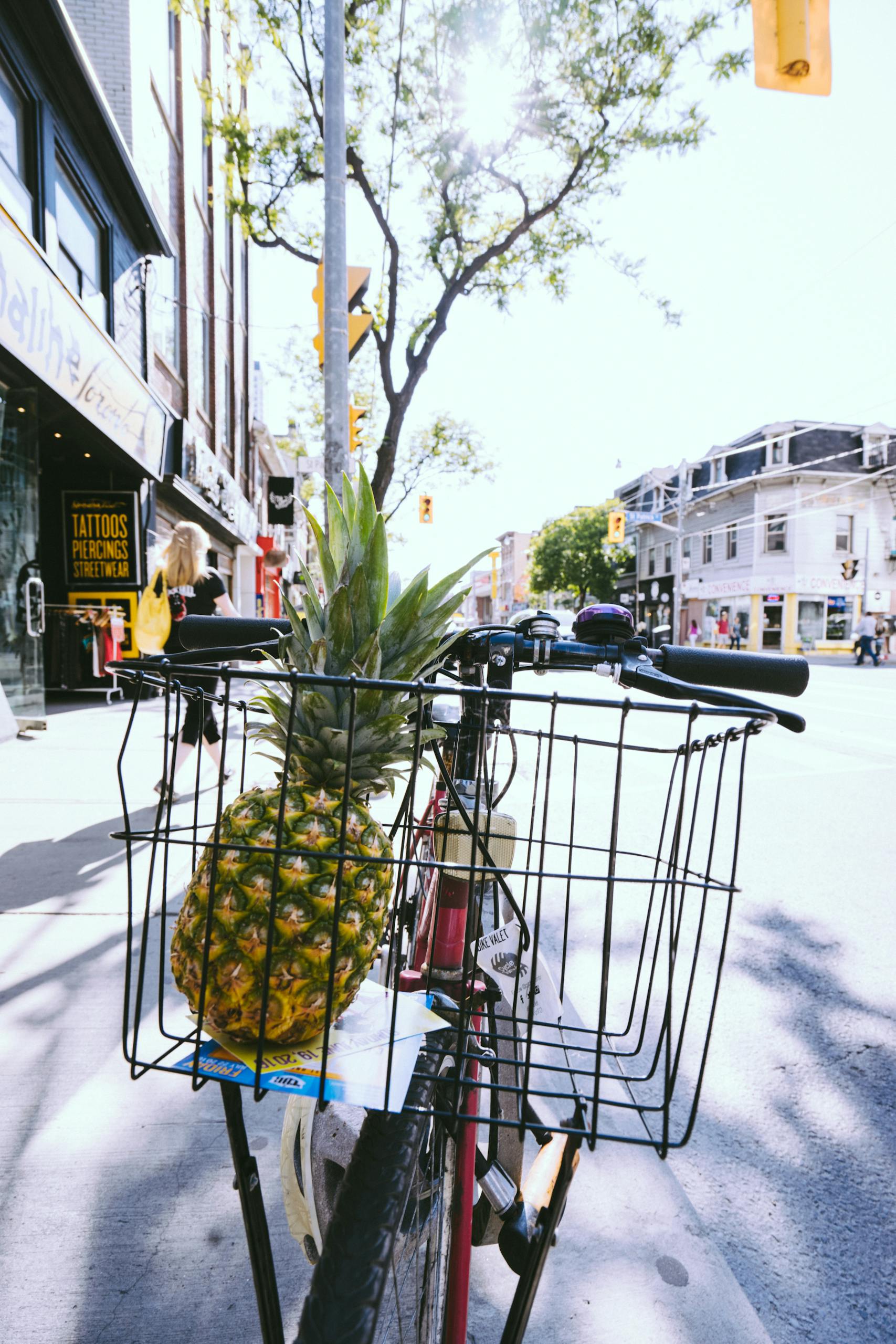 Pineapple in bike basket on a sunny day in a lively urban street scene.